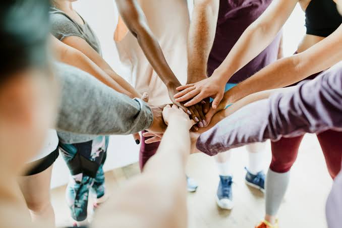 A diverse group placing their hands together in a team huddle, symbolizing community and unity